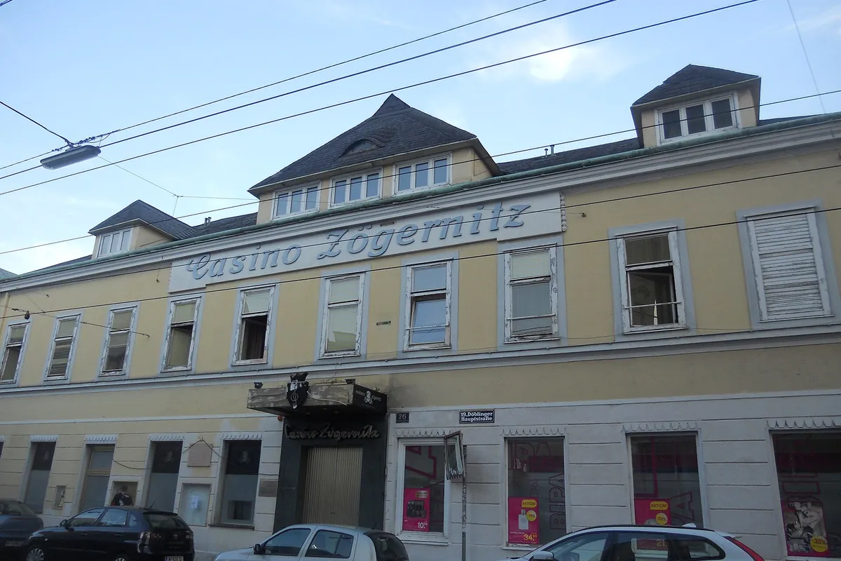 A yellow and cream four-storey building on a street with tram wires overhead, with the name Casino Zögernitz in raised letters below the roofline
